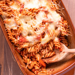 Fusilli pasta casserole with mozzarella cheese and tomato and wooden spoon, top view, close-up