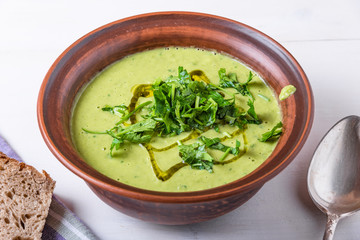Pea cream soup sprinkled with sliced parsley and olive oil in a clay plate and pieces of bread on a light background, top view, close-up...