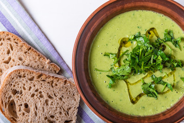 Pea cream soup sprinkled with sliced parsley and olive oil in a clay plate and pieces of bread on a light background, top view, close-up...