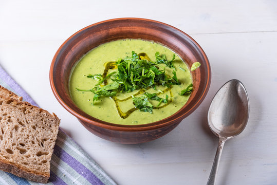 Pea cream soup sprinkled with sliced parsley in a clay plate and pieces of bread on a light background, top view