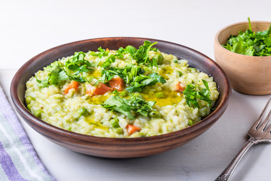 Traditional Italian vegetarian risotto with peas, carrots and parsley in rustic style, closeup
