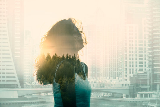 Double exposure with young woman in the modern cityscape and forest.