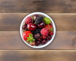 Top view. Fruits and berries in bowl on wooden background. Ripe currants, raspberries, cherries, strawberries, gooseberries, blackberries, mulberries, gooseberries. 