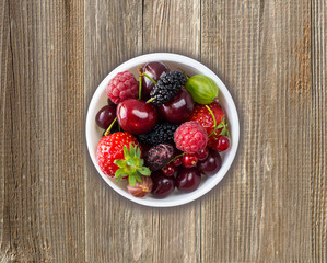 Fruits and berries in bowl on wooden background. Mix berries on rustic background. 