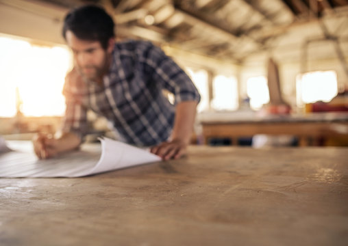 Craftsman leaning on a workshop bench reading furniture plans
