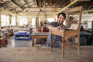 Smiling furniture maker sanding a chair in his woodworking shop