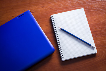 Blue laptop with notebook and pencil on the wooden table