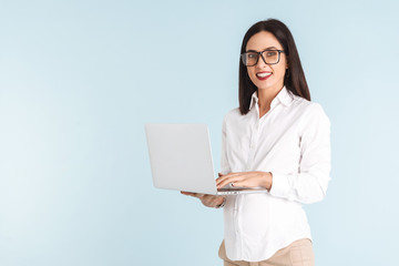 Pregnant business woman isolated over blue wall background using laptop computer.