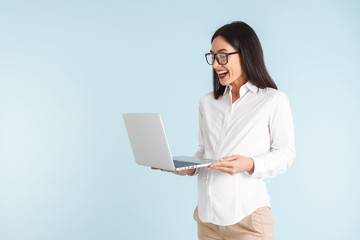 Beautiful shocked young business woman isolated over blue wall background using laptop computer.