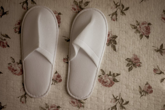 White towelling hotel disposable slippers over old and rust bed-sheet. Old and classic vintage style with noise and grains added.