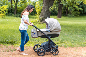 A beautiful young mother walking with her baby in a stroller in the park on a sunny day. - 244545076