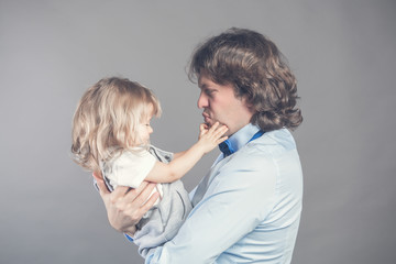 Happy smiling father holding on hands preschool daughter, looking at each other, father standing on grey studio background together with little girl. Daddy playing and embracing his loved toddler girl