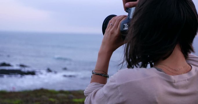 Young female photographer taking picture of beautiful ocean landscape - close up from behind