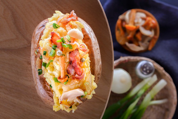 Baked potatoes with bacon, mushrooms and green onions in a rustic style on a wooden board. Close-up. Top view