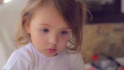 Little girl three years old with blond hair relish lunch chewing food and tell something.