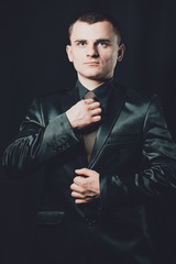 young stylish guy dressed in black classic suit on a black background