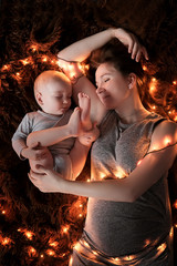 A young mother and her baby are sleeping on a fluffy brown blanket, lights are spread around them