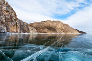 Frozen Lake Baikal. Beautiful smooth blue ice with cracks near the famous Sagan-Zaba bay with ancient rock paintings on the white-marble rocks