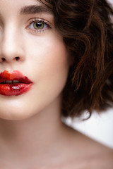 Closeup macro portrait of female face. Human woman half-face with unusual beauty makeup. Girl with perfect skin, green pistachio colour eyes and scarlet red lips make-up.