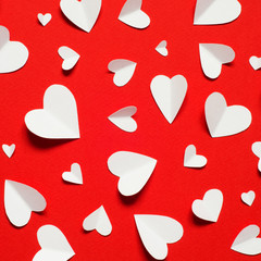 Valentine's day romantic background. White paper hearts at red backdrop, top view.
