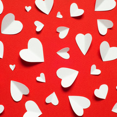 Valentine's day romantic background. White paper hearts at red backdrop, top view.