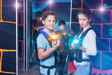 Cheerful teen girl and boy with laser pistols playing laser tag