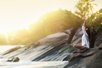 Woman Yoga Meditates on a Rock on the Ocean Beach in the Sunlight