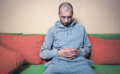 Lonely and depressed man feeling anxious and without reason for life sitting alone on his bed in...