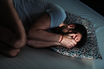 Young depressed man in pain on the bed