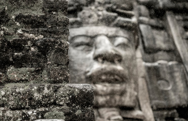 View of the wall of the Mayan temple of Lamanai, with out of focus stone face in background.
