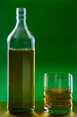 Bottle and glass with whiskey on a green golden background.