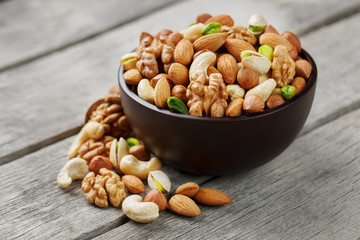 Wooden bowl with mixed nuts on a wooden gray background. Walnut, pistachios, almonds, hazelnuts and cashews, walnut.