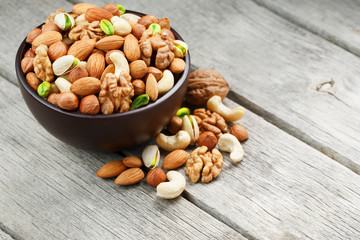 Wooden bowl with mixed nuts on a wooden gray background. Walnut, pistachios, almonds, hazelnuts and...