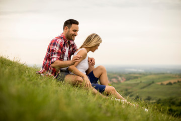 Naklejka na ściany i meble Loving couple sitting hugged on grass in the mountain