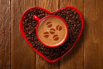 Red cup and coffee saucer in heart shape with decorated coffee on old wood background. Top View. grain shape in coffee.