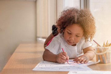 Little toddler girl laying down concentrate on drawing.  Mix African girl learn and play in the pre-school class. Children enjoy hand writing. 3 years girl enjoy playing at nursery. - obrazy, fototapety, plakaty