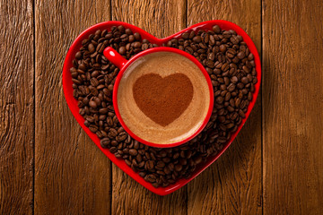 Red cup and coffee saucer in heart shape with decorated coffee on old wood background. Top View. Heart shape in coffee.