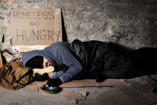 Houseless man sleeping on the street with alms box