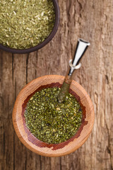 Traditional South American Yerba Mate tea in wooden mate cup with bombilla metal straw serving as a sieve, photographed overhead (Selective Focus on the tea in the cup)