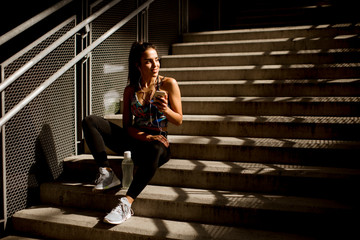 Young fit sporty woman resting and listen music on mobile phone after training outdoor on stairs in urban enviroment