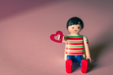 Toy holding a Valentine's Day red heart on pink background