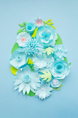 Easter egg made of paper flowers on blue background. Cut from paper.