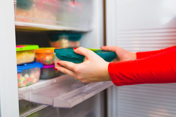 Woman placing container with frozen mixed vegetables in refrigerator. - obrazy, fototapety, plakaty