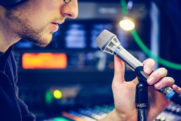 Studio recording: Young man with headphones speaks into a microphone, studio in the blurry...