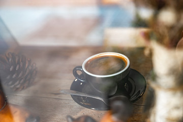 close up hot black coffee in black cup on wooden table, through window view