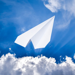 White paper airplane in a blue sky with clouds. The message symb