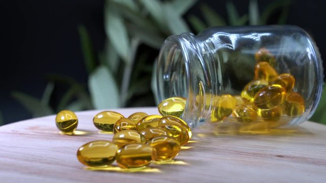 Shallow DOF soft gel capsules spilled from bottle. Vitamins supplements pills omega 3 on table in rotation. 3840X2160 UHD 4k.