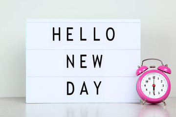 Lightbox with words Hello New Day with alarm clock on grey background