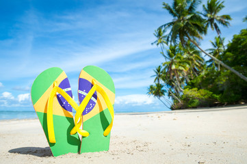 Brazil flag flip-flops standing in the sand on the shore of a palm-fringed Brazilian beach 