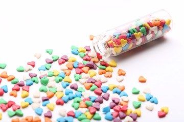 Colorful heart shaped sprinkles with glass bottle on white background